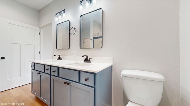 bathroom featuring double vanity, a sink, toilet, and wood finished floors