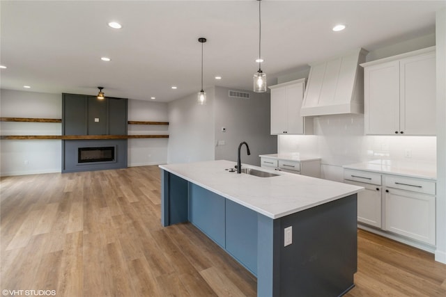 202 Meadowlark Dr, Monroe, IA 50170 - kitchen featuring premium range hood, white cabinets, light wood-type flooring, a kitchen island with sink, and recessed lighting