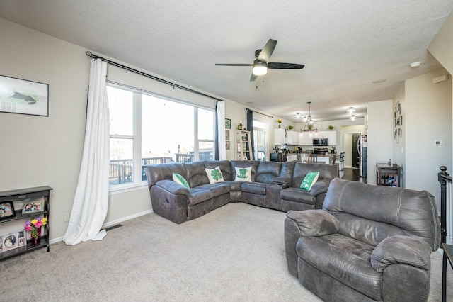 living area featuring visible vents, a textured ceiling, carpet flooring, baseboards, and ceiling fan