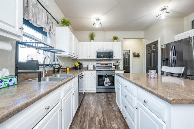 kitchen with dark wood-style flooring, white cabinetry, stainless steel appliances, and a sink