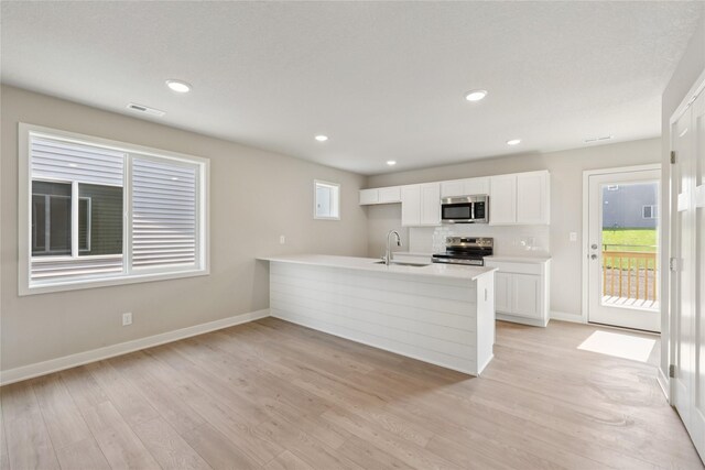 2917 Jerry St, Van Meter, IA 50261 - kitchen with stainless steel appliances, a peninsula, white cabinetry, light countertops, and light wood-style flooring