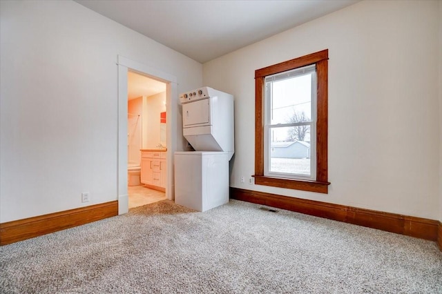 carpeted spare room featuring stacked washer / dryer and baseboards