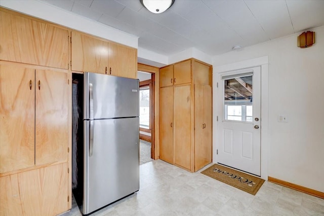 kitchen featuring light floors, baseboards, freestanding refrigerator, and light brown cabinetry