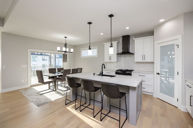 kitchen featuring a breakfast bar area, light wood finished floors, a sink, gas range oven, and wall chimney exhaust hood