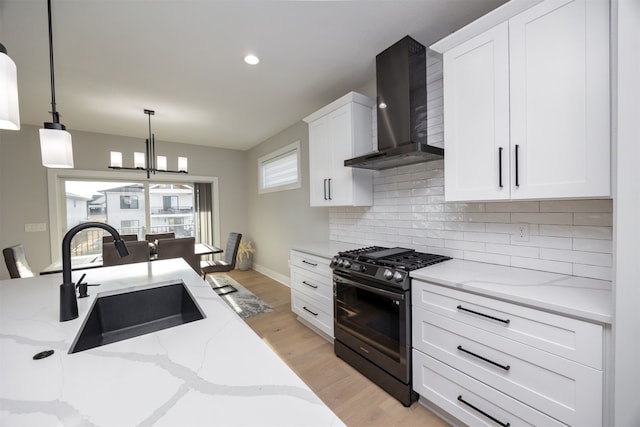 kitchen featuring a sink, range with gas cooktop, wall chimney exhaust hood, white cabinets, and decorative backsplash