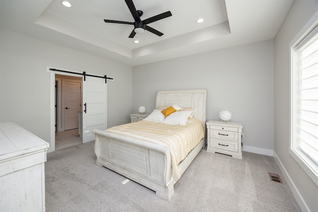 bedroom featuring a barn door, light colored carpet, and a raised ceiling