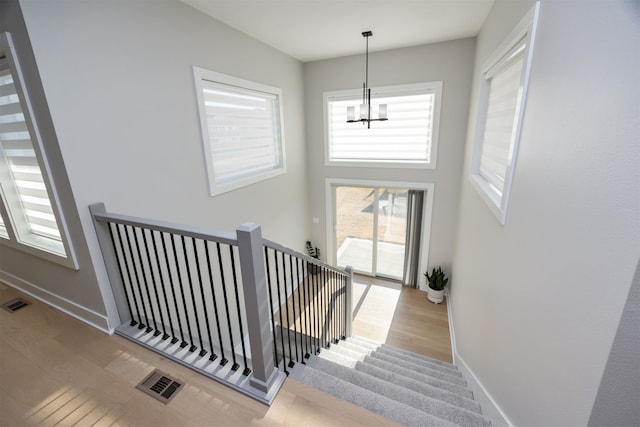 stairs featuring visible vents, an inviting chandelier, baseboards, and wood finished floors