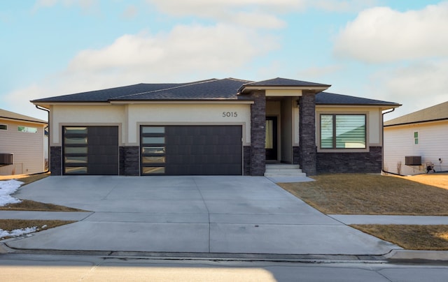 prairie-style house with stone siding, stucco siding, an attached garage, and driveway