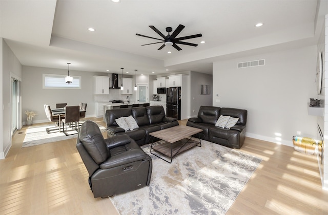 living room featuring visible vents, a raised ceiling, light wood-style floors, and baseboards