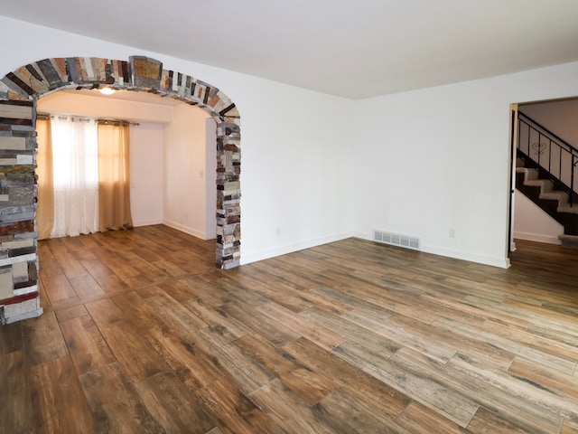 unfurnished living room with arched walkways, visible vents, wood finished floors, and stairway