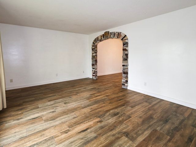empty room featuring baseboards, arched walkways, and wood finished floors