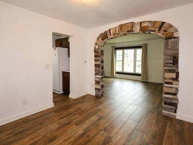 spare room featuring dark wood-style flooring, arched walkways, and baseboards