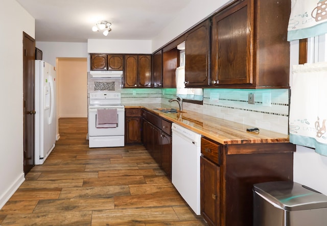 kitchen with dark brown cabinetry, backsplash, a sink, under cabinet range hood, and white appliances