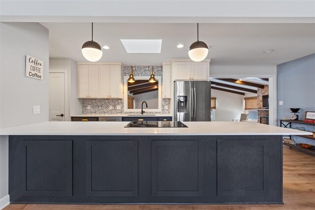 kitchen with light countertops, a skylight, stainless steel refrigerator with ice dispenser, black electric cooktop, and a sink