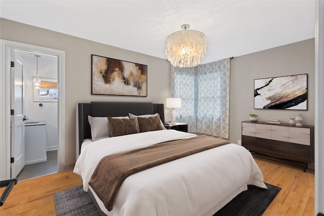 bedroom featuring light wood-type flooring, ensuite bathroom, and a chandelier