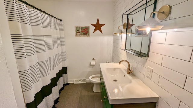 full bath with visible vents, toilet, tile walls, baseboards, and vanity