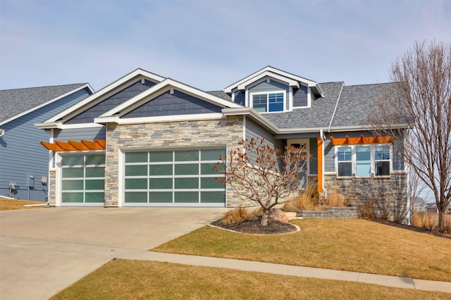 craftsman house with a front yard, driveway, a shingled roof, a garage, and stone siding