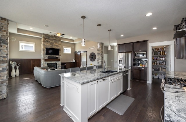 kitchen with light stone countertops, stainless steel appliances, a stone fireplace, a sink, and open floor plan