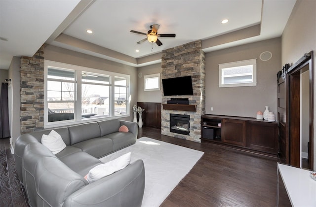 living area with a ceiling fan, a barn door, a fireplace, a raised ceiling, and dark wood-style flooring