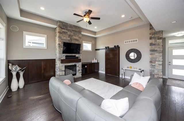 living area featuring a tray ceiling, a barn door, dark wood-type flooring, and visible vents