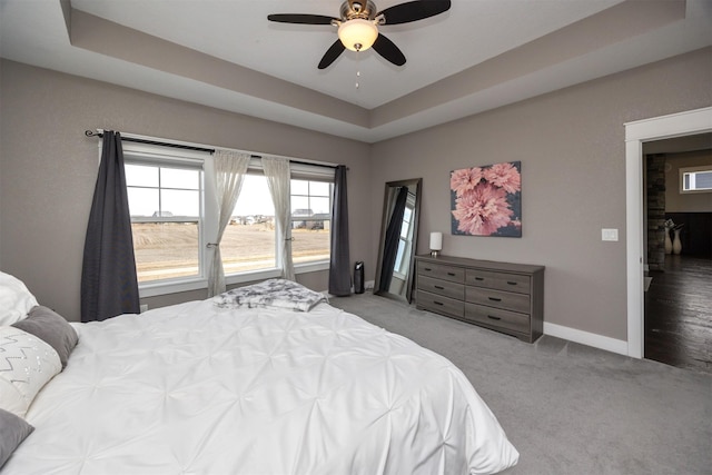 carpeted bedroom with a tray ceiling, baseboards, and ceiling fan