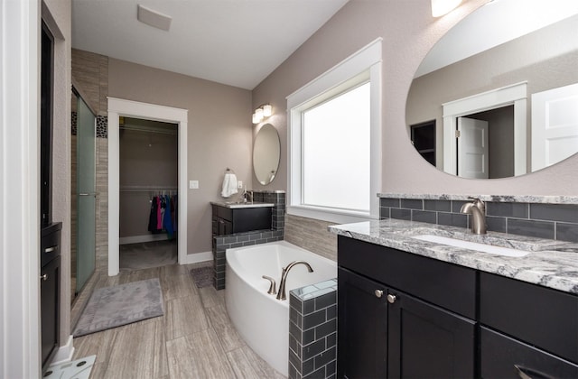 full bath with a walk in closet, two vanities, a stall shower, a sink, and a bath