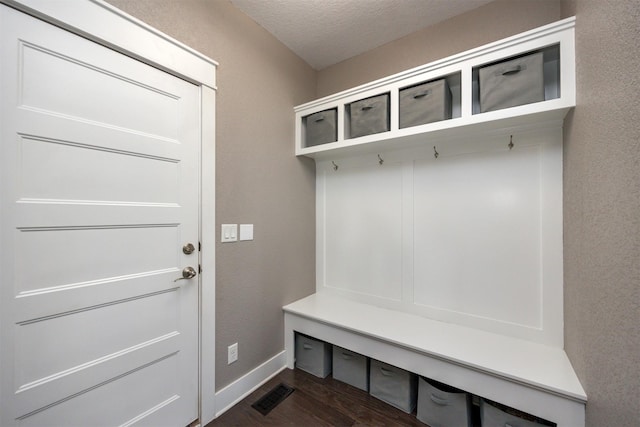 mudroom with dark wood finished floors, visible vents, a textured ceiling, and a textured wall