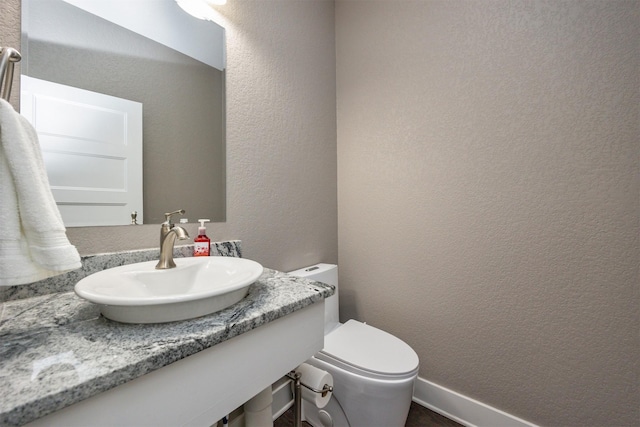 bathroom featuring toilet, a textured wall, and a sink