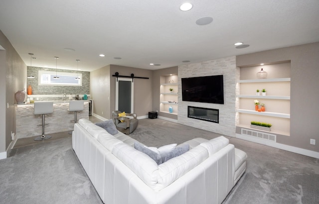 living room featuring built in shelves, a barn door, a large fireplace, baseboards, and light colored carpet