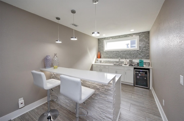 kitchen with visible vents, beverage cooler, a sink, a peninsula, and white cabinets