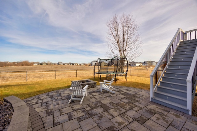 view of patio featuring stairway, a trampoline, fence, and a fire pit