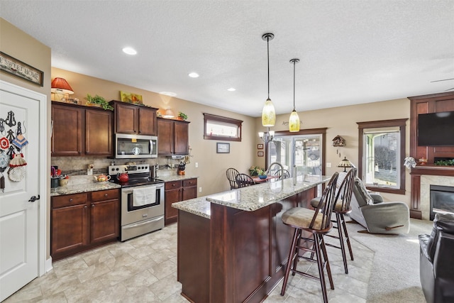 kitchen featuring light stone countertops, a fireplace, appliances with stainless steel finishes, a kitchen breakfast bar, and tasteful backsplash