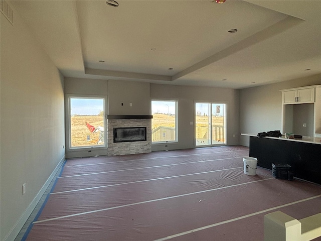 unfurnished living room with a wealth of natural light, a stone fireplace, baseboards, and a tray ceiling