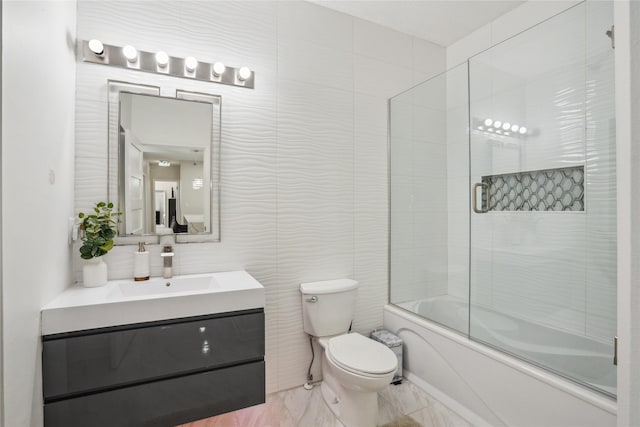 full bathroom featuring toilet, marble finish floor, tile walls, enclosed tub / shower combo, and vanity