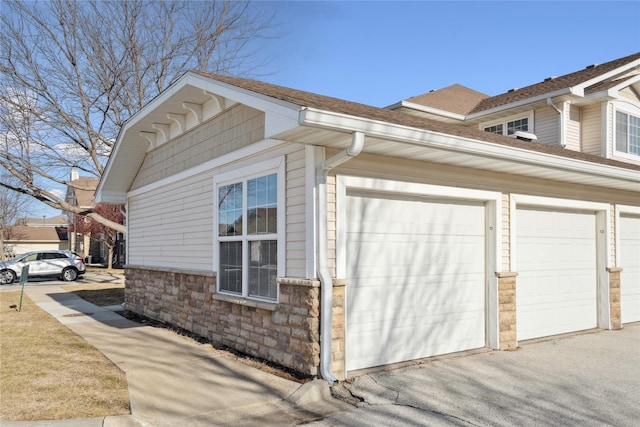 view of side of property featuring stone siding, driveway, and a shingled roof