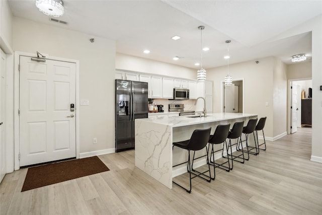 kitchen with a breakfast bar area, a sink, stainless steel appliances, white cabinets, and light wood-style floors