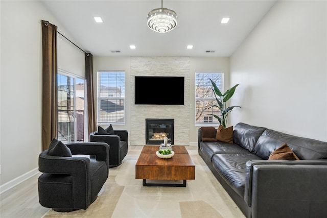 living area featuring a stone fireplace, visible vents, baseboards, and light wood finished floors