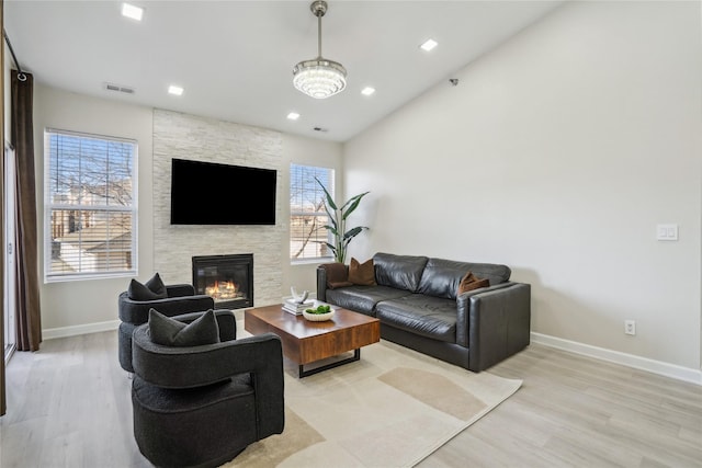 living area featuring visible vents, light wood-style flooring, recessed lighting, a stone fireplace, and baseboards