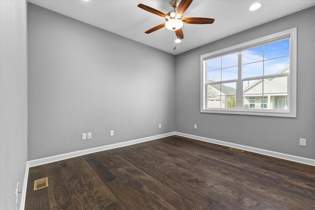 empty room with dark wood-style floors, visible vents, a ceiling fan, and baseboards