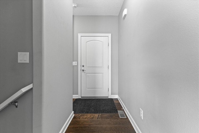 doorway with dark wood-style floors, visible vents, a textured ceiling, and baseboards