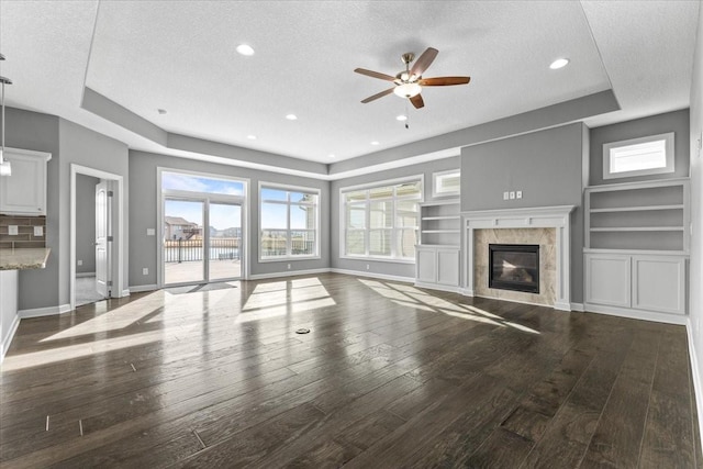 unfurnished living room featuring a fireplace, baseboards, a tray ceiling, and hardwood / wood-style flooring