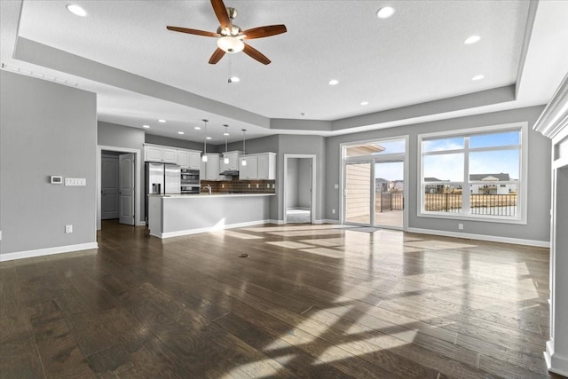 unfurnished living room with recessed lighting, a tray ceiling, baseboards, and dark wood-type flooring