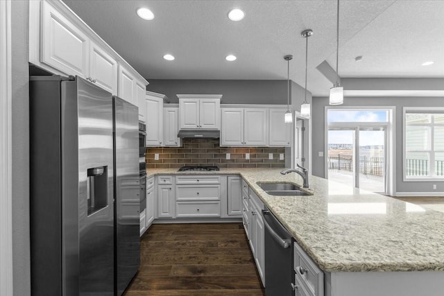 kitchen with appliances with stainless steel finishes, a peninsula, dark wood-style floors, white cabinets, and a sink