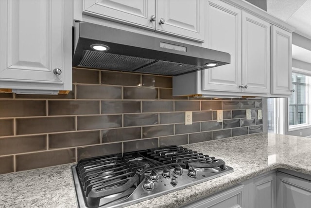 kitchen featuring decorative backsplash, stainless steel gas stovetop, white cabinets, and under cabinet range hood