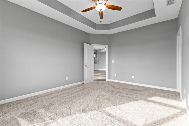 spare room featuring baseboards, visible vents, carpet floors, ceiling fan, and a raised ceiling