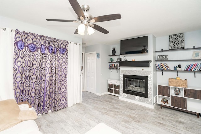 living room with a ceiling fan, wood finished floors, baseboards, and a tile fireplace