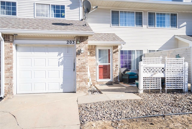 entrance to property with a garage, brick siding, roof with shingles, and driveway