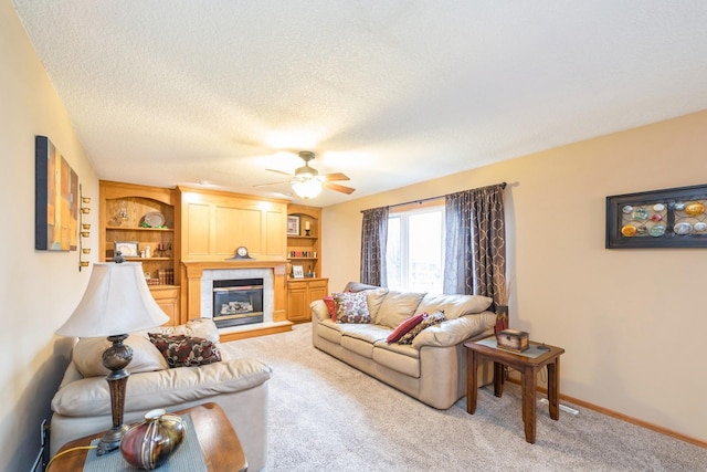 living area featuring baseboards, ceiling fan, a tile fireplace, a textured ceiling, and light colored carpet