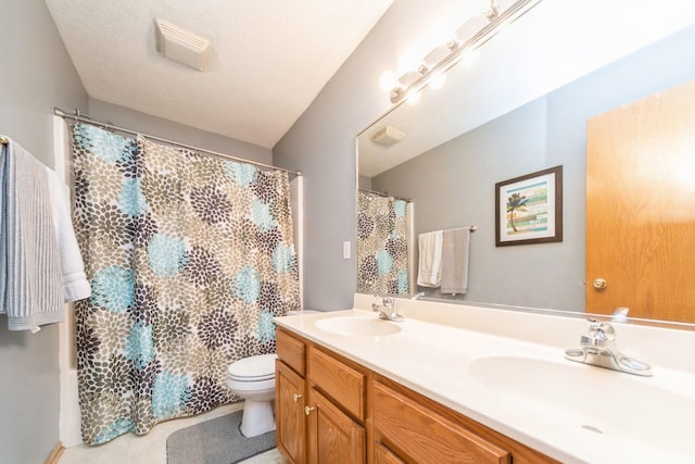 bathroom featuring a textured ceiling, double vanity, toilet, and a sink