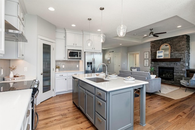 kitchen with a sink, stainless steel appliances, white cabinets, light wood-style floors, and wall chimney range hood